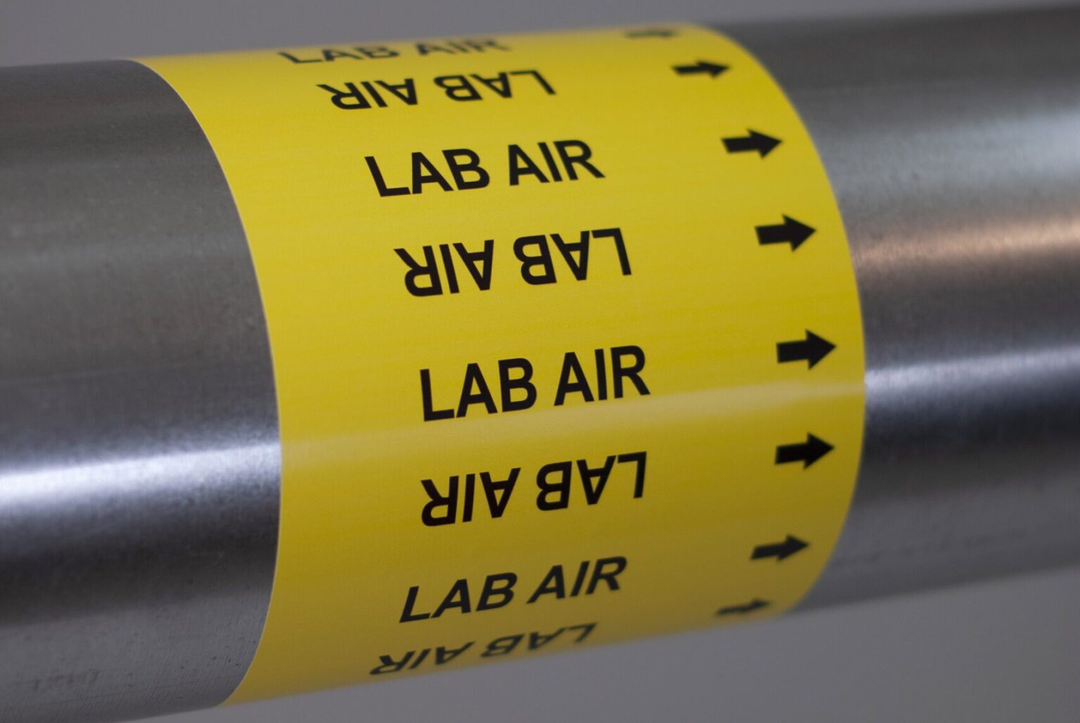 A yellow Medical pipe marker wraps around a steel pipe the marker reads lab air with an arrow pointing to the right