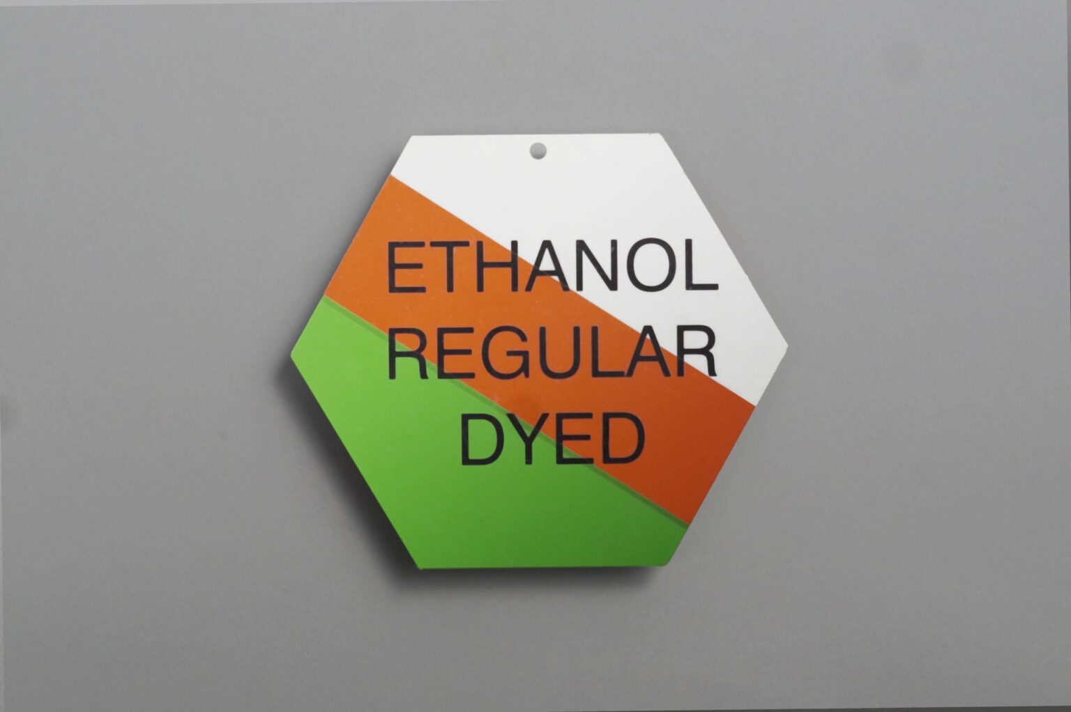 A hexagon shaped valve tag splits in three colors white An orange stripe in the middle And green at the bottom. The text reads "ethanol regular died"